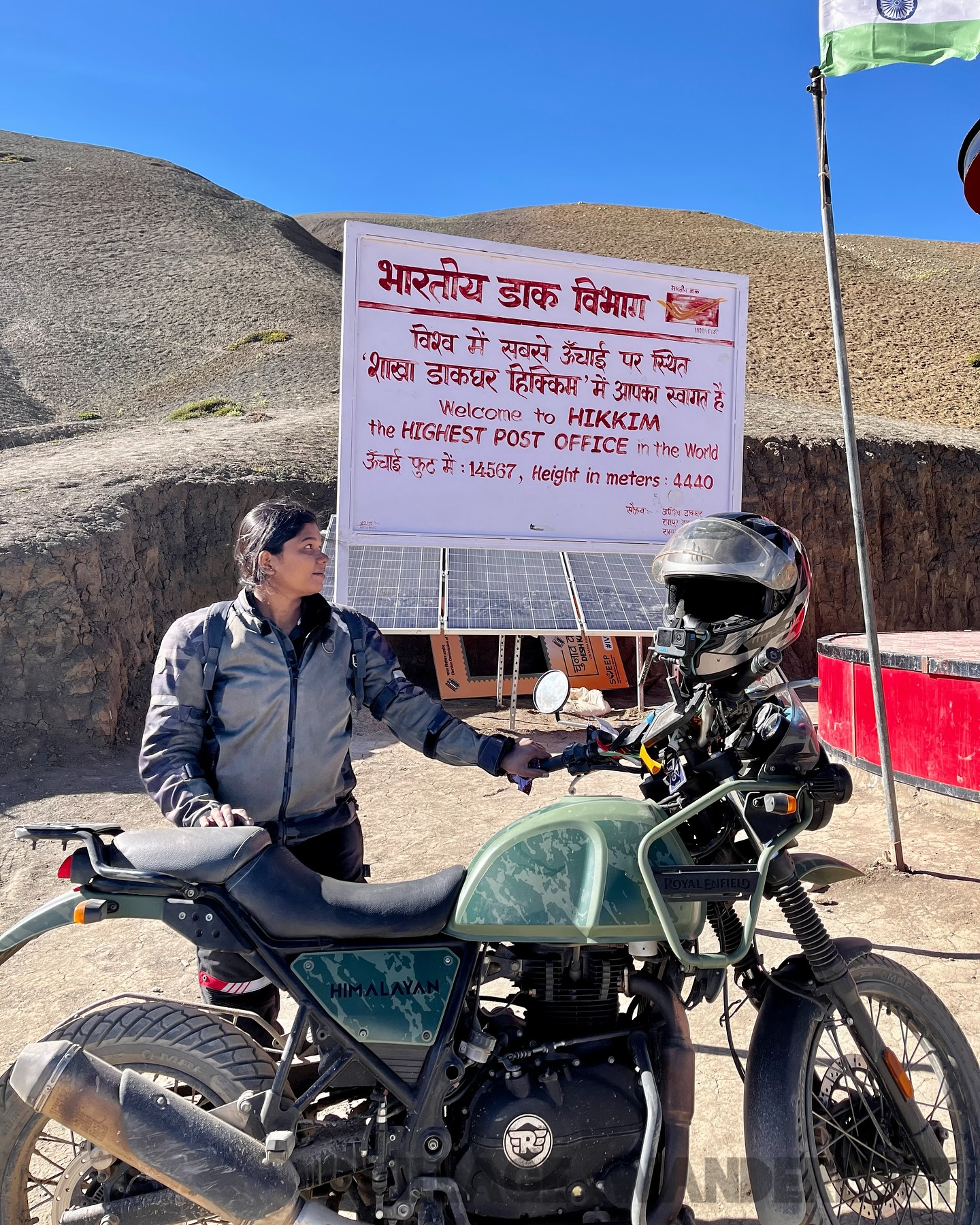 Thenmozhi with her motorcycle beside the Hikkim Post Office sign in Spiti Valley.