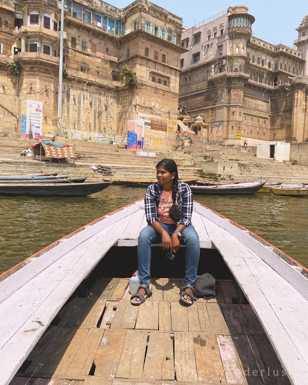 Thenmozhi seated in a boat on the Ganga with the historic ghats of Varanasi behind her.